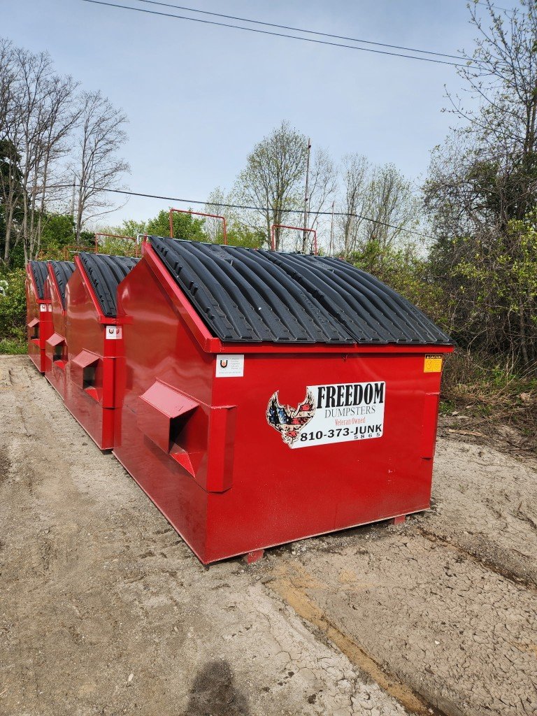 Row of red Freedom Dumpsters front-load containers with black lids and company branding for scheduled business pickup